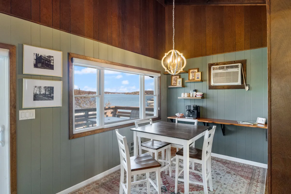 A cozy dining area with a dining table situated by a large window that frames a scenic view. Decorative light fixtures and wall art lend a welcoming atmosphere, perfect for family meals and morning coffee.