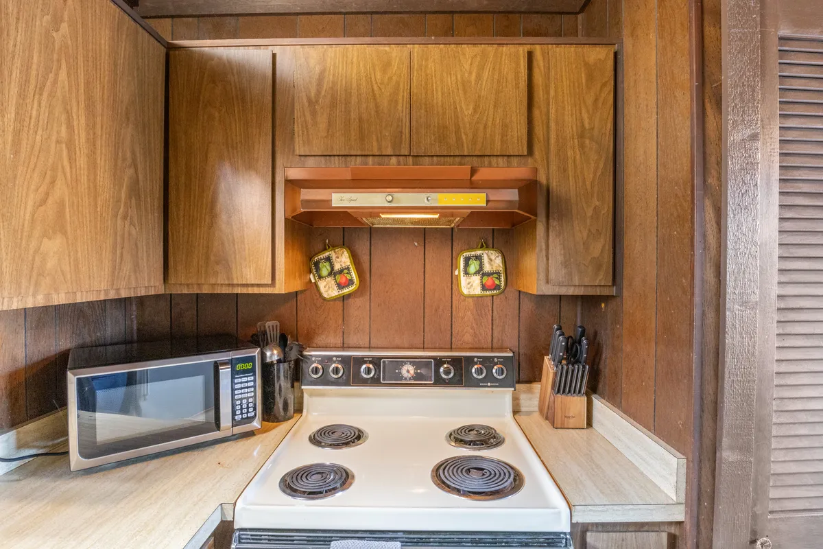 A close-up of the kitchen's cooking area, featuring a stove, microwave, wooden cabinets, and kitchen utensils arranged neatly. The space feels nostalgic and practical, suitable for both quick snacks and hearty meals.