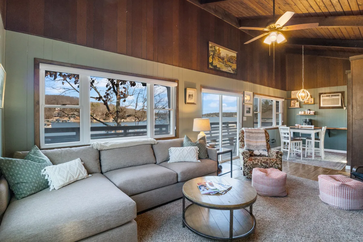 A wide-angle view of the open concept living and dining area. The photo showcases a comfortable sectional sofa, a light-filled dining area, and decorative lighting fixtures. The seamless connection between the seating and dining spaces is apparent, reinforcing the cabin’s social, family-friendly layout.