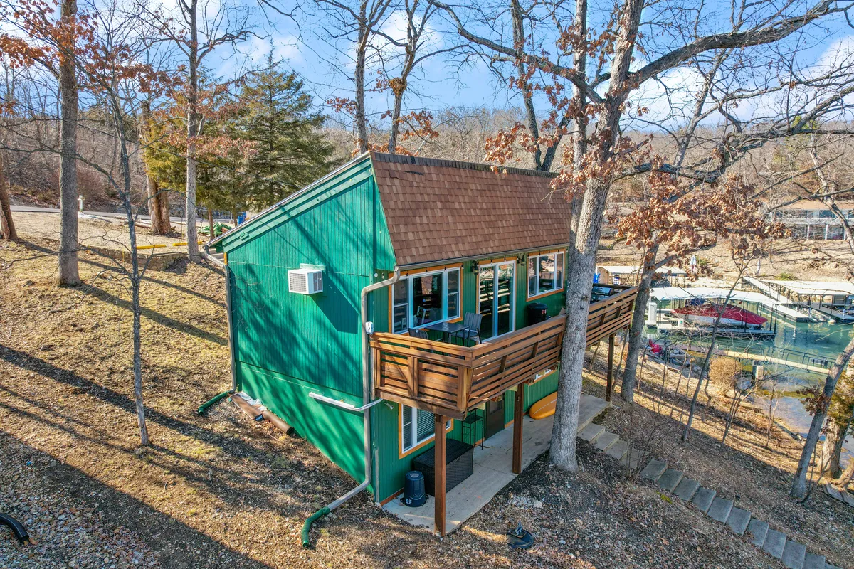 This image shows the inviting green exterior of Red Trout Cabin with a wooden balcony nestled among trees. Outdoor furniture hints at a spot for relaxing with morning coffee. The ambiance is tranquil and connected to nature, reflecting the porch's role as the transition from indoors to the lakeside experience.