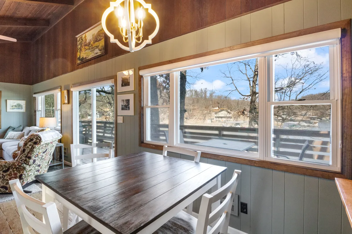 The dining area, with a welcoming table set beneath a chandelier, is surrounded by windows that let in natural light. The view includes both the dining table and lounge seating, with wall art and a cozy, intimate atmosphere ideal for family meals or evenings in.