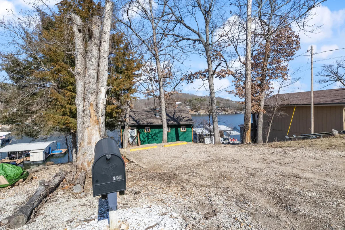 This exterior image shows a green lakeside house with a mailbox in the foreground and sweeping views of the water, bordered by trees. The peaceful lakeside environment sets the perfect atmosphere for pet-friendly outdoor adventures, portraying an ideal spot for walks and relaxation with your furry companion.