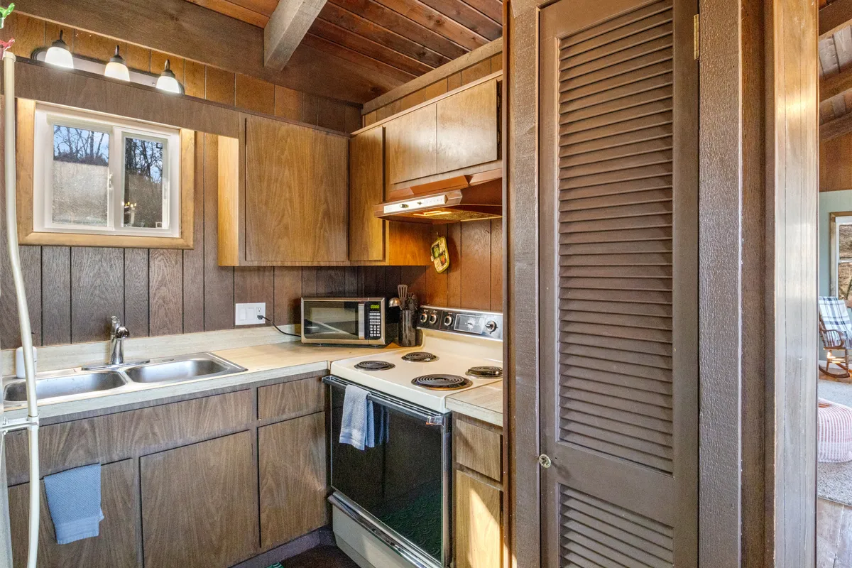 A warmly lit kitchen with visible appliances, ample countertop space, wood paneling, and a window letting in natural light. The setup is both functional and inviting, ideal for everyday cooking and casual family meal prep.