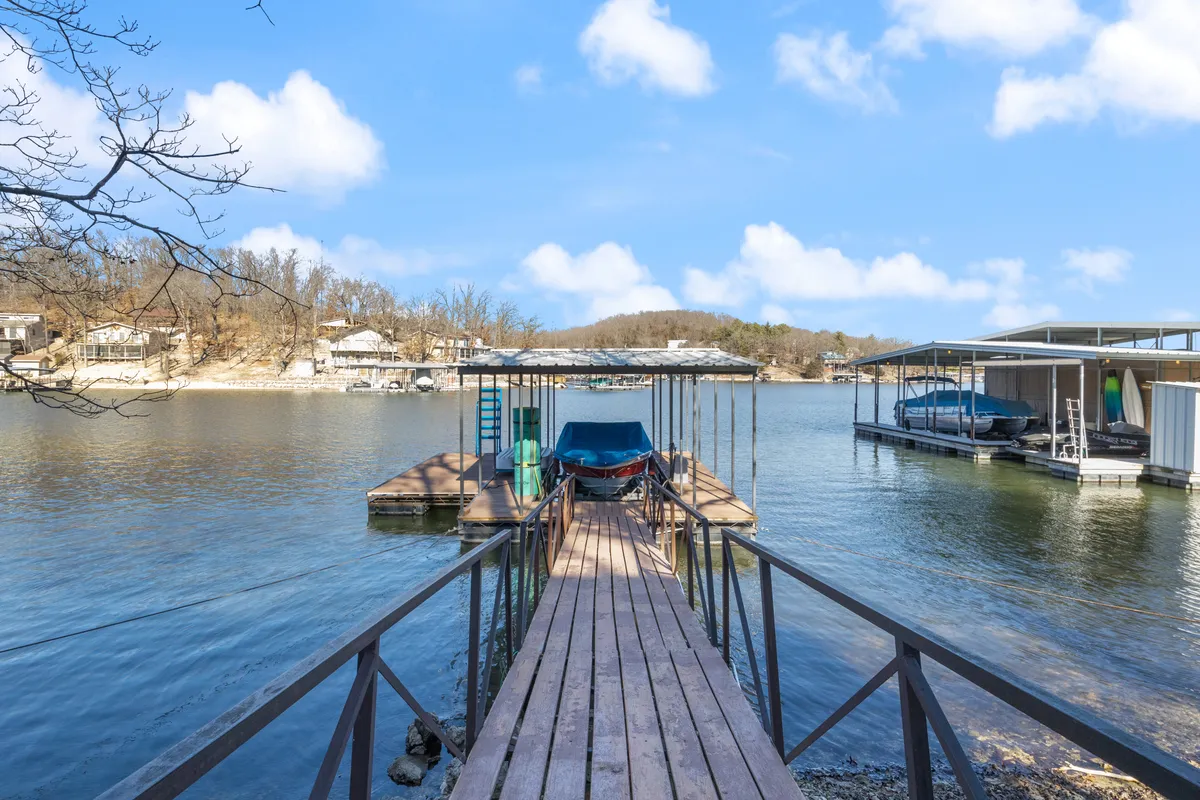 The image showcases a tranquil lakeside setting with a wooden dock extending over calm water, moored boats, and soft golden sunlight reflecting off the surface—hinting at both sunrise and sunset views. The peaceful shoreline and inviting dock foreground a perfect environment for fishing, boating, or simply relaxing by the water.
