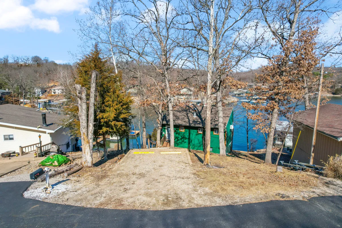 An exterior shot featuring a lake view, a green building nestled among trees, and an open driveway. The tranquil scene highlights ample space for outdoor activities, from lakeside walks to sunset watching, while subtly tying in the comfort and privacy of cabin living.