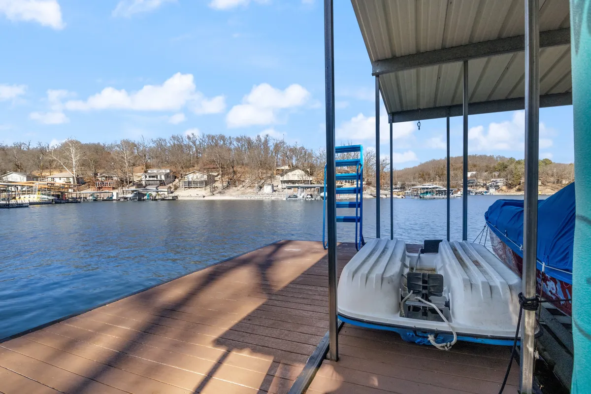 A peaceful dock scene with boats moored, clear water, and distant hillside homes. The image captures the expansive dock area, perfect for fishing, boating, swimming, and relaxing by the lake.